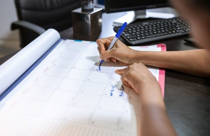 Person trägt Termine mit blauem Stift in einen Tischkalender ein