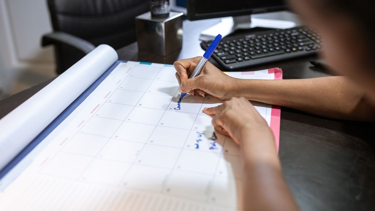 Person trägt Termine mit blauem Stift in einen Tischkalender ein