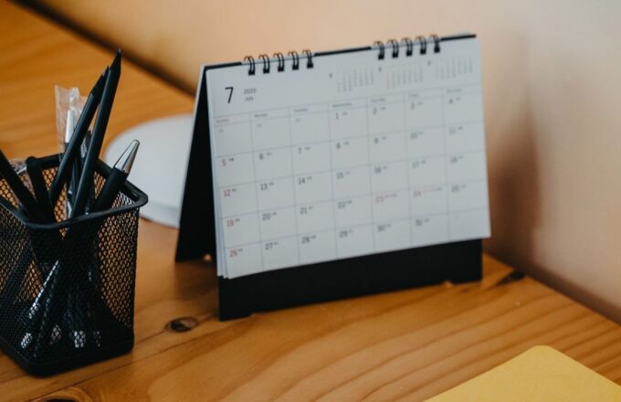 Tischkalender, Stiftebecher, Notizbuch und Laptop auf einem Holzschreibtisch