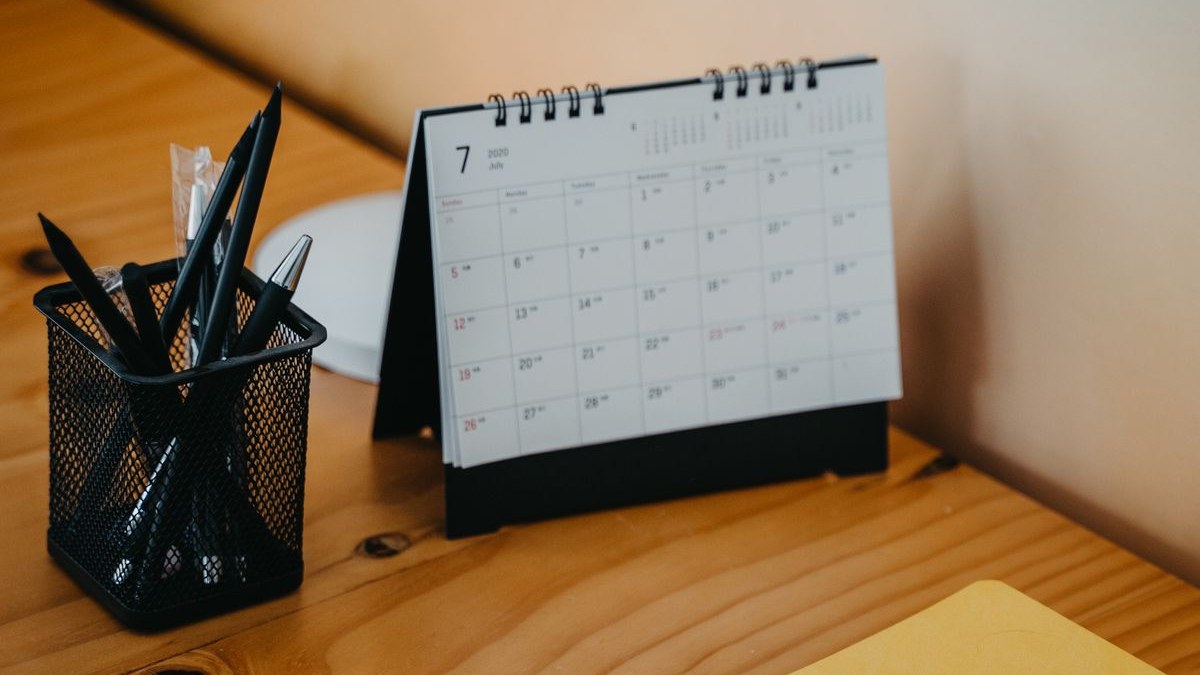 Tischkalender, Stiftebecher, Notizbuch und Laptop auf einem Holzschreibtisch
