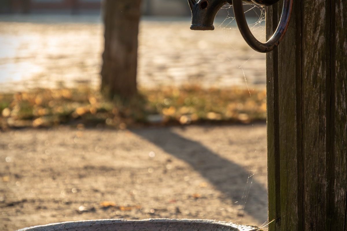 Alte Schwengelpumpe aus Metall mit steinernem Becken