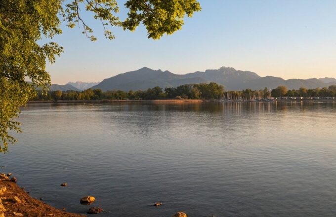 Chiemsee im Abendlicht mit Bäumen am Ufer und den Chiemgauer Alpen im Hintergrund