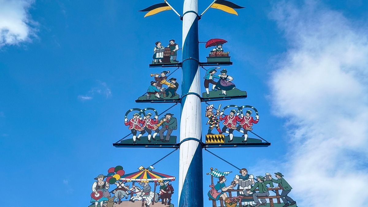 Weiß-blauer Maibaum in München mit bemalten Figuren aus Brauchtum, Musik und Festen vor blauem Himmel