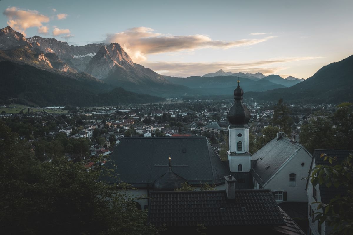 Blick über Garmisch-Partenkirchen mit Kirchturm und Alpen im Abendlicht