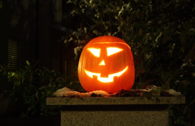 Leuchtender Halloween-Kürbis mit geschnitztem Gesicht auf einem Steinsockel bei Nacht