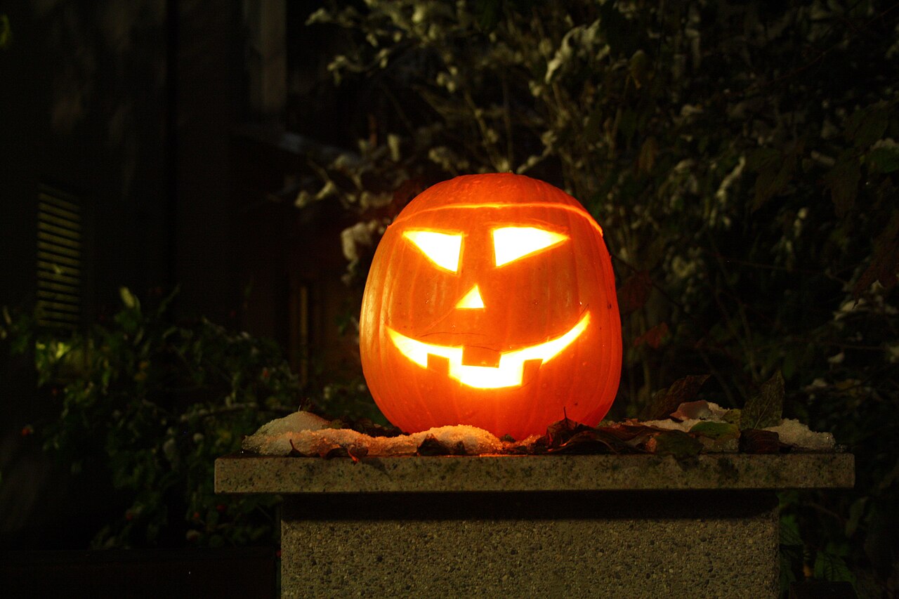 Leuchtender Halloween-Kürbis mit geschnitztem Gesicht auf einem Steinsockel bei Nacht