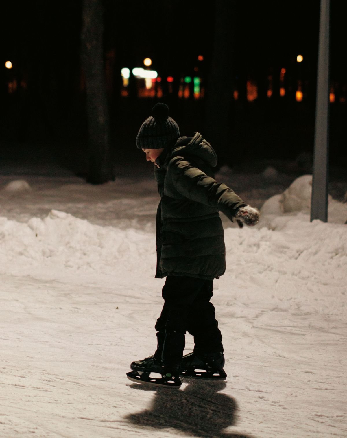 Kind lernt Schlittschuhlaufen auf einer Eisbahn am Abend