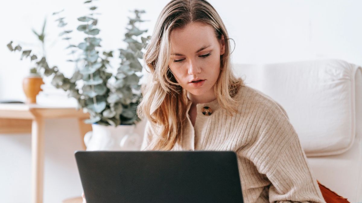 Selbstständige Frau arbeitet konzentriert am Laptop in ihrer Wohnung