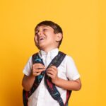 Kind mit Schulranzen vor gelbem Hintergrund